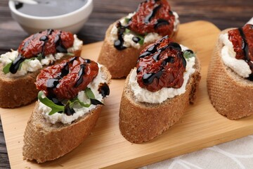 Delicious bruschettas with sun-dried tomatoes, cream cheese and balsamic vinegar on table, closeup