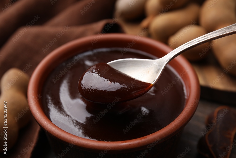 Wall mural taking tasty tamarind sauce with spoon from bowl on table, closeup