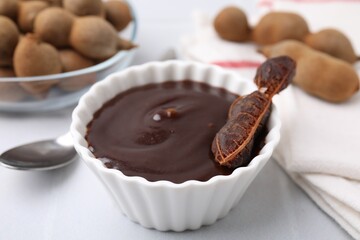 Bowl of tamarind sauce and fresh pods on light table, closeup