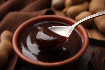 Taking tasty tamarind sauce with spoon from bowl on table, closeup - obrazy, fototapety, plakaty