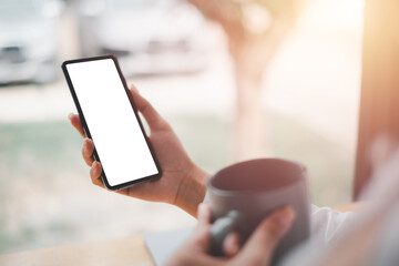 Cell phone Mockup image blank white screen, woman hand holding texting using mobile on desk at coffee shop, background empty space for advertise text.