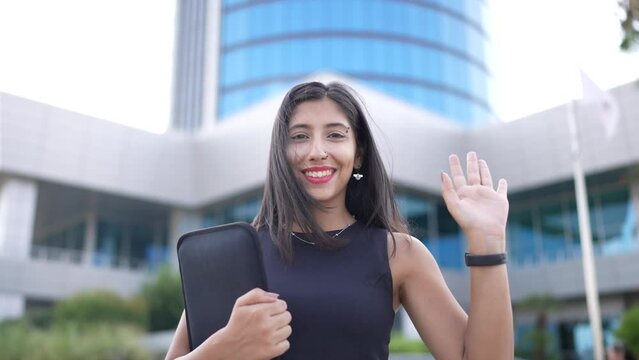 Close-up portrait of nice-looking multi-race brunette beautiful elegant young business woman carrying a case looking into camera and waving hand. Daily people life, fashion, beauty. Female portraits.