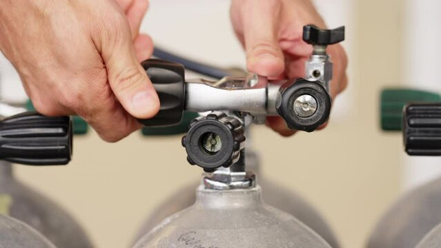 Person filling compressed air in scuba dive tank with compressor in dive center