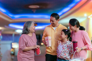 Family, parents, children and grandma holding popcorn and drinking water chatting cheerfully before the movie.