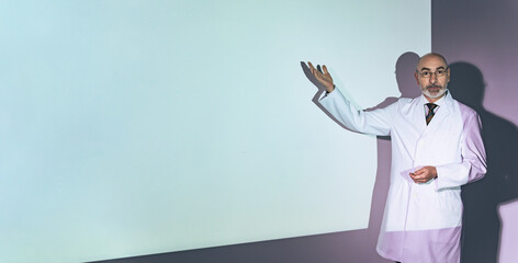 Senior Caucasian man wearing a white coat giving a presentation on a projector.