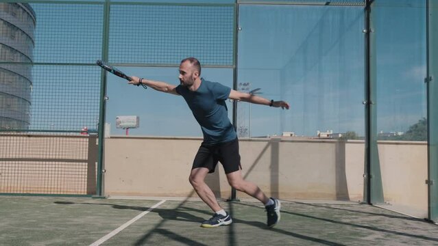 Padel tennis player does a low handback shot after the ball hits the backwall.