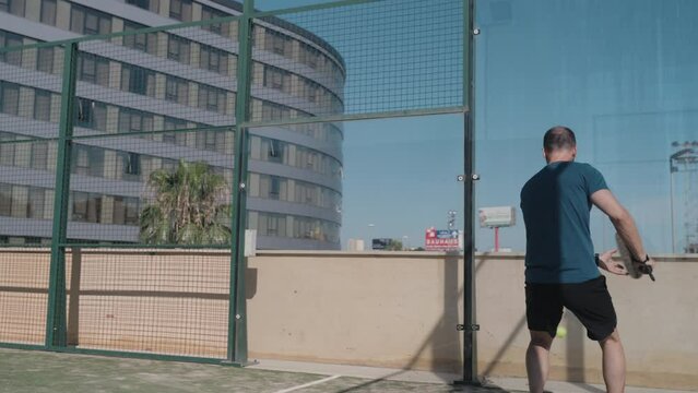 Padel tennis player hits the ball under his legs after ball hits the backwall.
