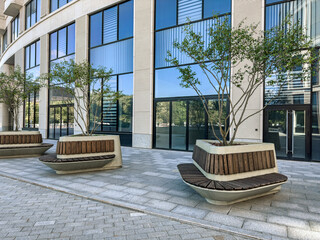 courtyard in an office buildings complex with green trees and benches for rest. - Powered by Adobe