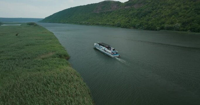 rlateral movement escort boat, behind a boat that moves on a river next to tall grass through high mountains to the side horizon