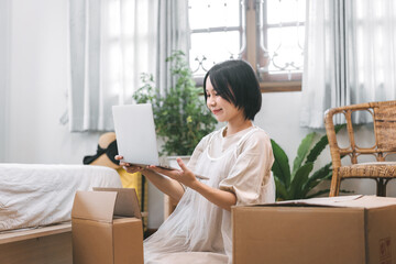 Asian woman unpack parcel box for new laptop in cozy bedroom