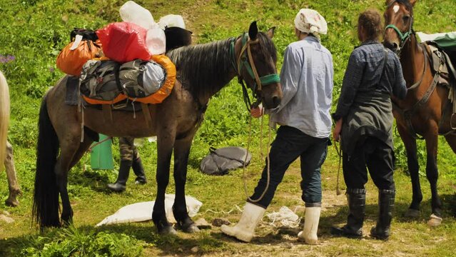 Man and woman chasseurs with horses loaded with hiking equipment. Close-up. View from the back. Packed horses ready to throw packs into the mountains