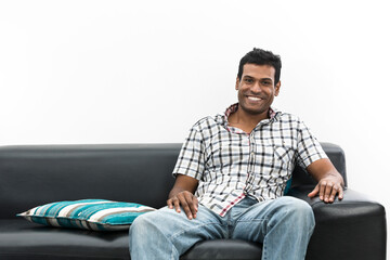 Happy young Indian man relaxing on sofa at home