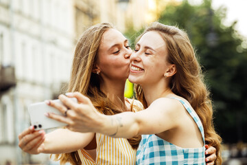 Two happy young women together taking a selfie in the city. Summer day.