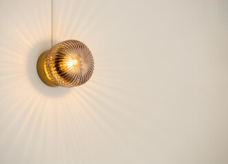 Close up round shape crystal light hanging on white wall in the interior room in cafe with copy space, minimal style. Small vintage crystal glass mounted wall lamp with refracting warm yellow light.