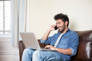 Indian Man using a laptop and phone at home.