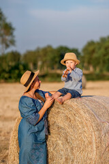 Naklejka na ściany i meble Happy Ukrainian mother with a child in a summer field on a haystack.
