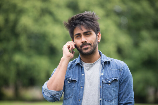 Asian Man standing in city park takling on mobile phone.