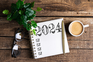 New year resolutions 2024 on desk. 2024 goals list with notebook, coffee cup, plant on wooden table. Resolutions, plan, goals, action, checklist, idea concept. New Year 2024 resolutions, copy space