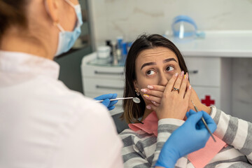 Woman afraid before dentisr procedure and covering mouth her hands, panic attack to pain