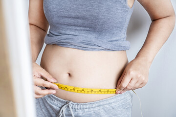 obese woman checking her fat  belly with a measuring tape, weight gain concept  - obrazy, fototapety, plakaty