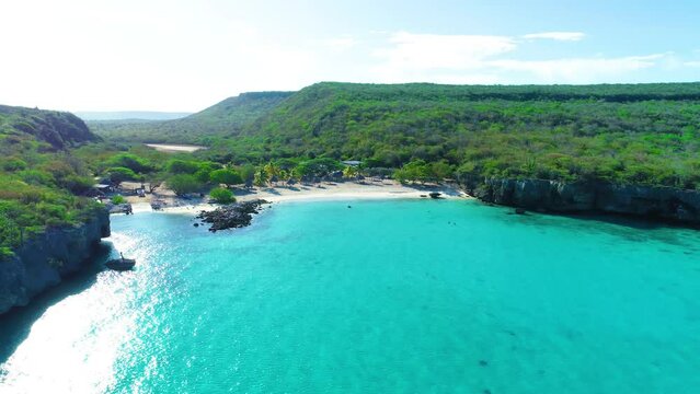 Drone rises above secluded white sandy tropical beach cove, curacao