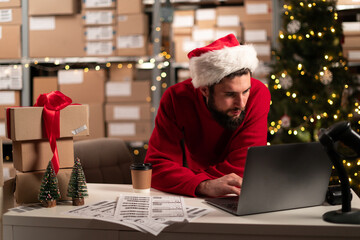 Male online store small business owner entrepreneur seller checking orders using laptop preparing delivery parcel on table. Christmas sale. Dropshipping concept.