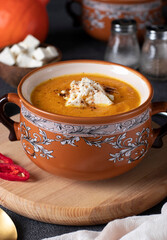 Pumpkin cream soup with feta cheese in brown bowl on wooden board