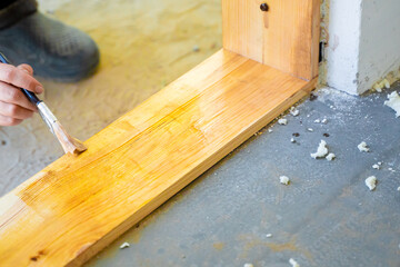 A woman's hand with a brush applies varnish to a wooden threshold of a door, close-up. Moisture...