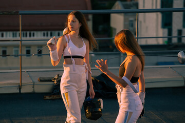 Two fencers woman practice on a rooftop with the city in the background.