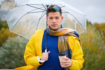 Young man wearing a yellow raincoat with a coffee and umbrella in street in autumn.