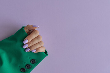 Female's hand with purple nails wearing green jacket on purple background. Gelish manicure - 634573106