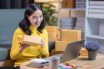 Startup small business entrepreneur or freelance Asian woman using a laptop with box in night, Young success Asian woman with her hand lift up, online marketing packaging box and delivery, SME concept