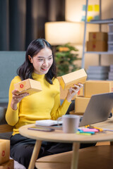 Startup small business entrepreneur or freelance Asian woman using a laptop with box in night, Young success Asian woman with her hand lift up, online marketing packaging box and delivery, SME concept