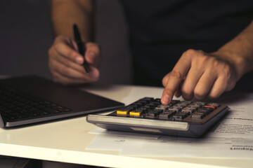 Asian man is using a calculator to calculate his monthly miscellaneous expenses at home. - obrazy, fototapety, plakaty