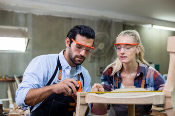 young carpenter man and women using measuring tape looking wood size at workspace. craftsman profession in wood factory.