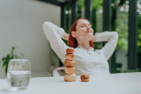 Stack of wooden pebbles on desk with businesswoman relaxing in background