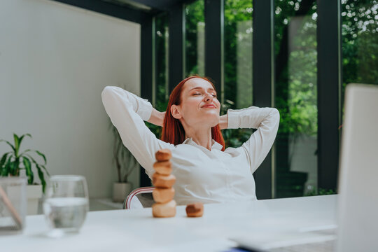 Smiling businesswoman relaxing with hands behind head at desk in office