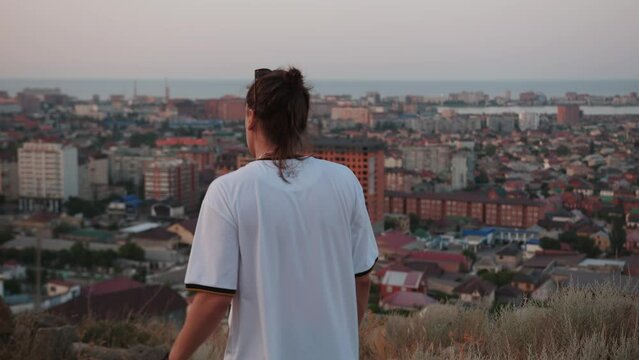 Young man hipster goes by mountain overlooking city on seashore. Slow motion