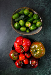 Assorted tomatoes and cucumbers of different colors and sizes on dark green table. Top view. Fresh vegetables harvest