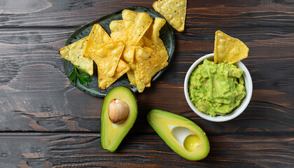 Fresh guacamole dip with chips on dark wooden background. Food and vegetarian concept. Top view.