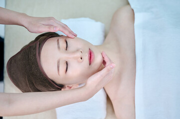 Fototapeta na wymiar 아시아 한국의 젊은 한국여성 모델은 스파 또는 피부관리전문점 또는 피부과 병원에서 침대에 누워서 전문관리사에게 머리와 얼굴을 관리를 받음. 최상전망사진