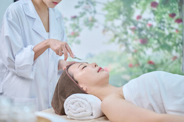 아시아 한국의 젊은 한국여성 모델은 스파 또는 피부관리전문점 또는 피부과 병원에서 침대에 누워서 전문관리사에게 초음파 스크래퍼로 피부관리를 받음.