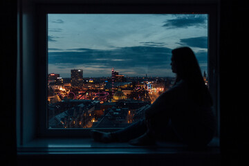 Young woman at window with city in background