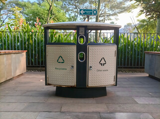 Two cream-colored trash bins with general waste and recycling with a garden background on public...