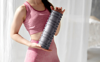 Grey foam roller massager held by a sportswoman. Sports inventory, tools. Lymphatic drainage...