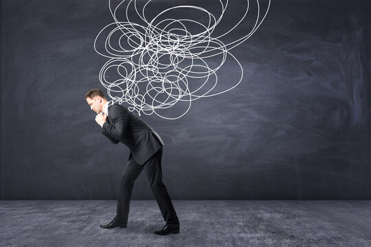 Stress burden and mental problems concept with tired businessman carrying heavy tangled line on blackboard background