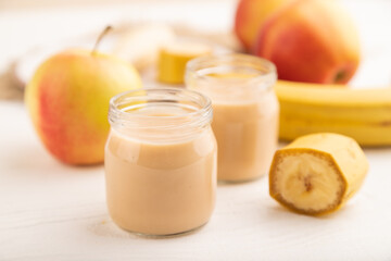 Baby puree with fruits mix, apple, banana infant formula in glass jar on white, side view, selective focus