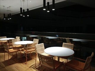 Modern interior design in a building room with Low light photography at night. Tables and chairs under the light with dark background.