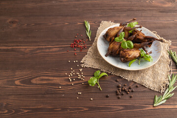 Smoked quails on a ceramic plate on a brown wooden background. Side view, copy space.