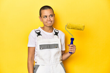 Painter woman, shaved head, with yellow roller in studio confused, feels doubtful and unsure.